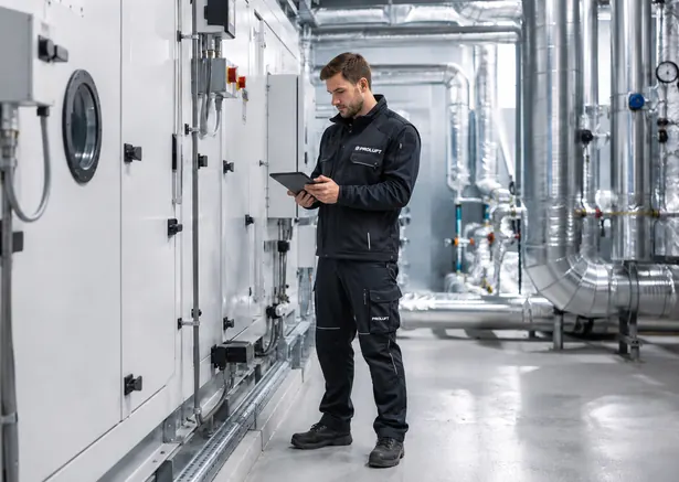 Proluft-Techniker prüft mit einem Tablet eine Lüftungsanlage im Technikraum